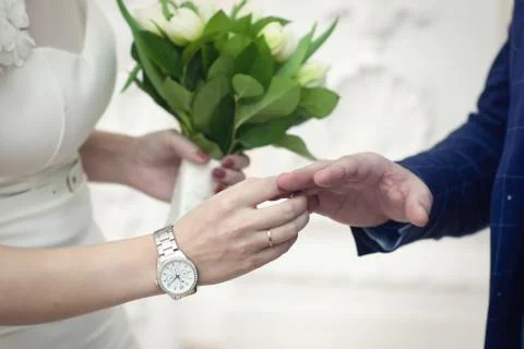 Lovers exchange rings. Close-up on a light background. The bride has a white  Stock Photos