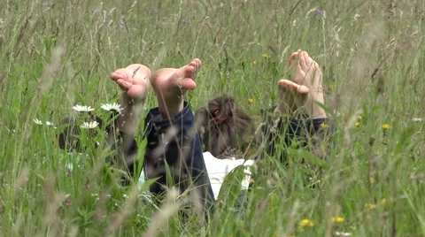 Lovers  lie down on green grass, playing with soles  Stock Footage 46208397