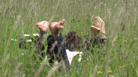 Lovers lie down on green grass, playing with soles 4K Stock Footage 46221440