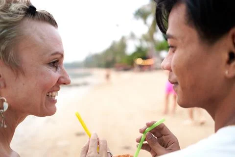 Lovers looking to each other while sharing a coconut juice in the beach Stock Photos