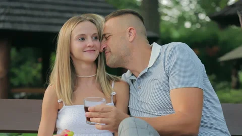 Lovers on a park bench in summer. A man sniffs a girl's hair. Cheerful mood and Stock Footage 217676698