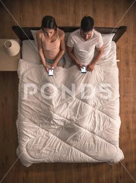 The lovers sit on the bed and phone. view from above Stock Photos
