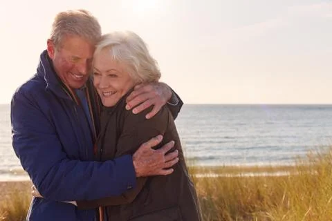 Loving Active Senior Couple Hugging As They Walk Through Sand Dunes Stock Photos
