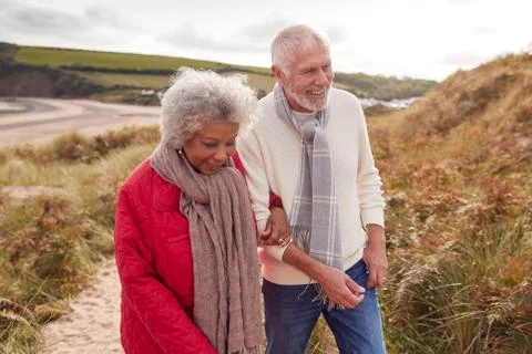 Loving Active Senior Couple Walking Arm In Arm Through Sand Dunes On Winter Stock Photos