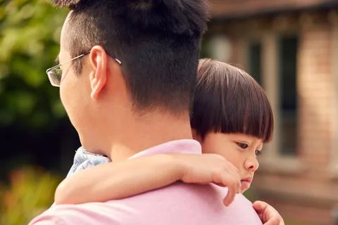 Loving Asian Father Cuddling Son In Garden As Boy Looks Over His Shoulder Stock Photos