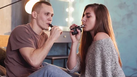 A loving couple on a bed smokes electronic cigarettes. Stock Footage 103160604