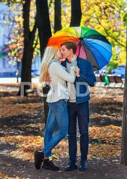 Loving couple on date under umbrella kissing in fall park. Stock Photos