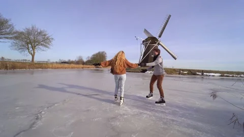 Loving couple having fun on ice in typical dutch landscape with windmill. Stock Footage 164928336