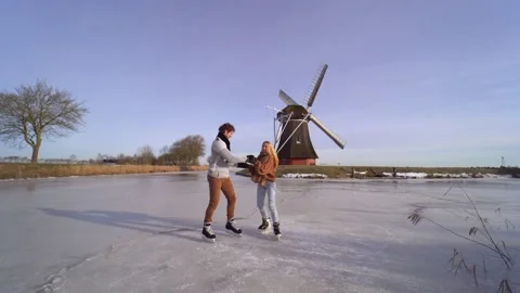 Loving couple having fun on ice in typical dutch landscape with windmill. Stock Footage 164928337
