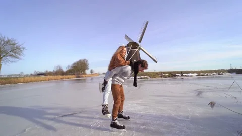 Loving couple having fun on ice in typical dutch landscape with windmill. Stock Footage 164928341
