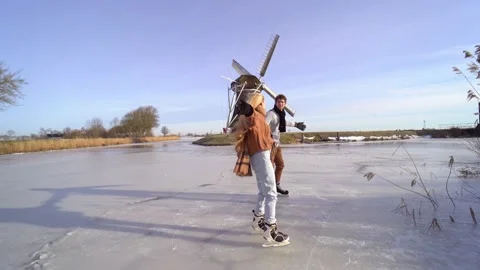 Loving couple having fun on ice in typical dutch landscape with windmill. Stock Footage 164928376