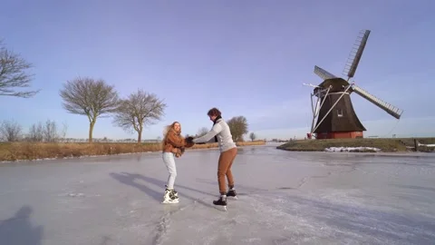 Loving couple having fun on ice in typical dutch landscape with windmill. Stock Footage 164928422