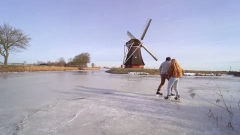 Loving couple having fun on ice in typical dutch landscape with windmill. Stock Footage 164928445