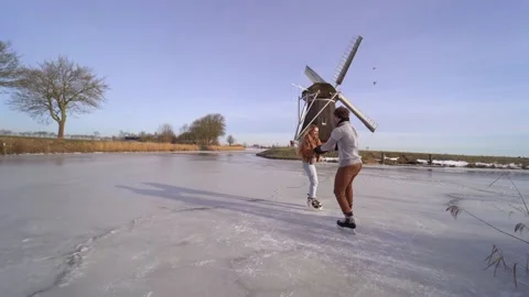 Loving couple having fun on ice in typical dutch landscape with windmill. Woman Stock Footage 225642331
