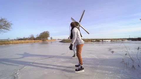 Loving couple having fun on ice in typical dutch landscape with windmill. Woman Stock Footage 225642364