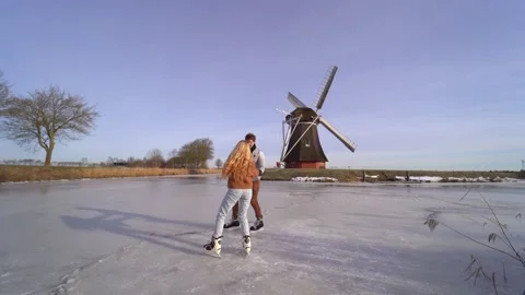 Loving couple having fun on ice in typical dutch landscape with windmill. Woman Stock Footage 225642449