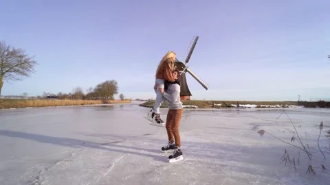 Loving couple having fun on ice in typical dutch landscape with windmill. Woman Stock Footage 225642487