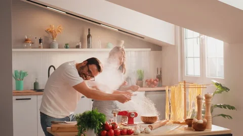 Loving couple having fun in the kitchen throwing flour at each other, laughing Stock Footage 235446425