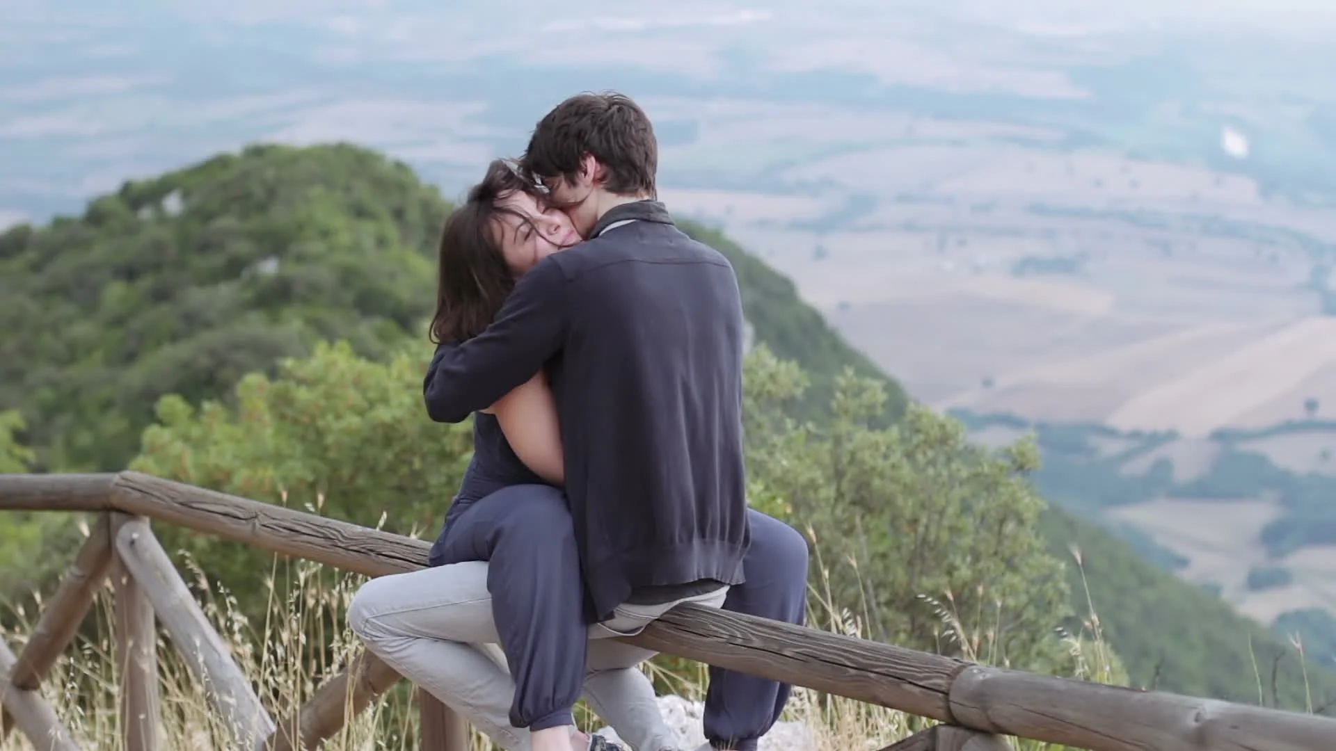 loving couple kissing sitting on a fence in the mountains,caresses