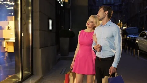 Loving couple looking at showcases with clothes discussing prices and models 스톡 동영상 80662664