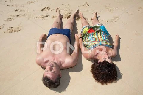 Loving couple lying on sand and holding hands Stock Photos