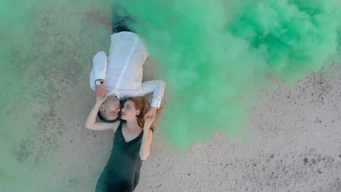 Loving couple lying on sandy shore. red-haired girl in a black dress and a guy Stock Footage 128460181
