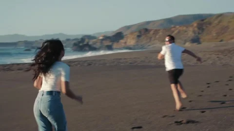 Loving couple playing on the beach running barefoot on the sand near the water 動画素材 323500257