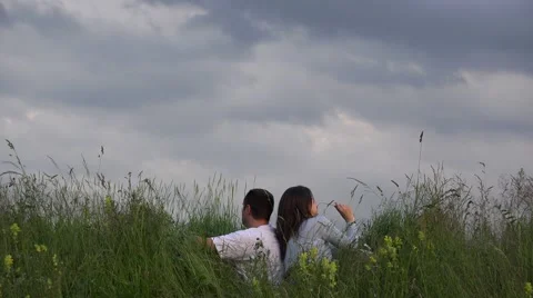 Loving couple sitting with back to each other, spring meadow, dramatic sky 4K Video stock 46206196