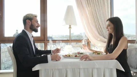 Loving couple sitting at a table in a restaurant, drinking wine and talking Stock Footage 130909974