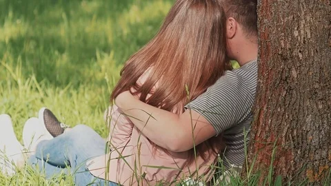 A loving couple together, hugging each other, sits under a tree in the park Stock Footage