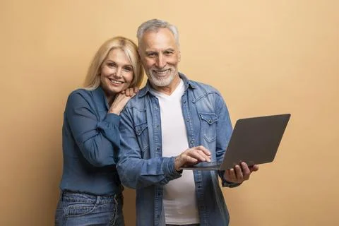 Loving elderly spouses using computer laptop on beige background Stock Photos