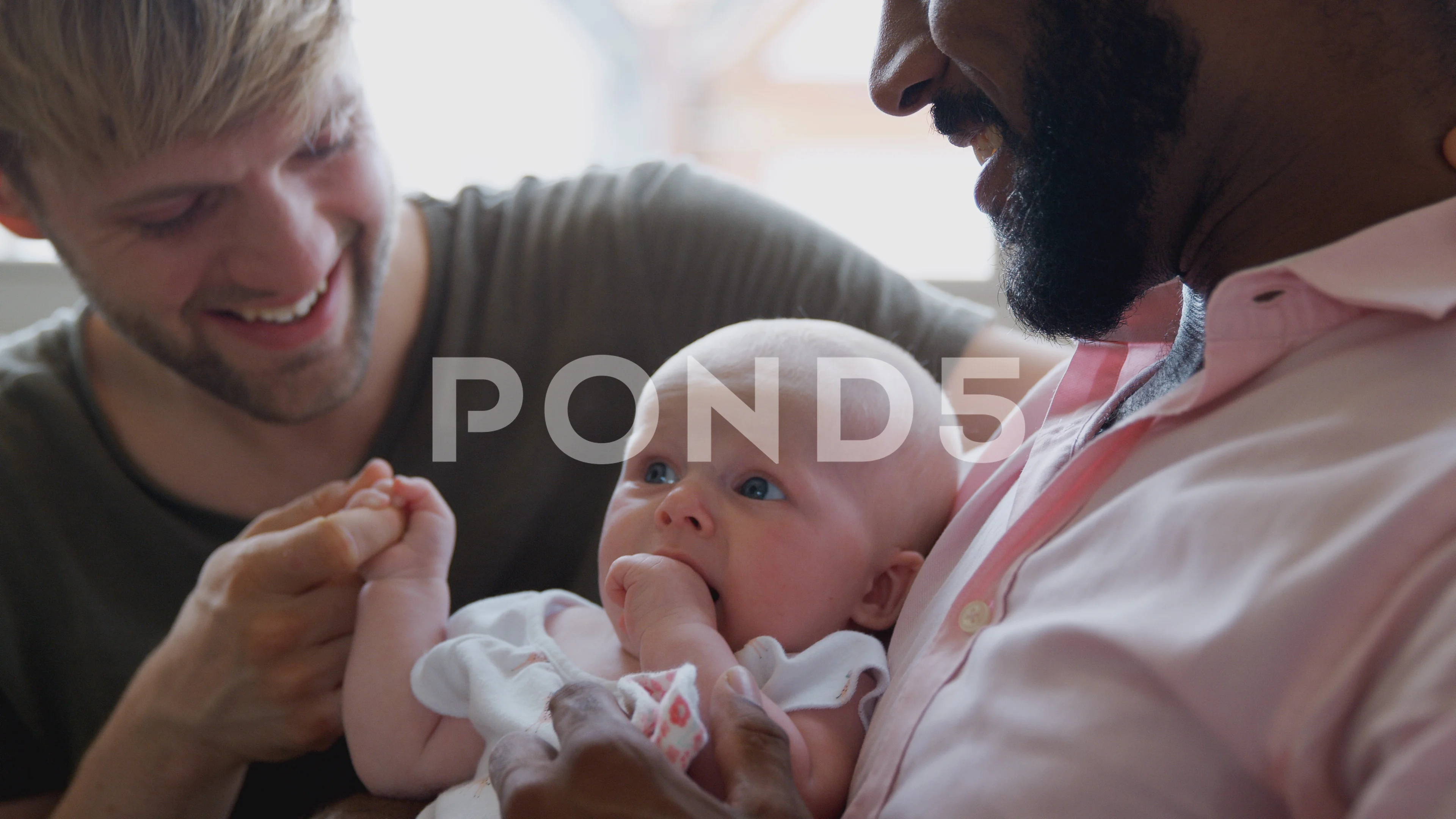 Loving Male Same Sex Couple Cuddling Baby Daughter On Sofa At Home Together