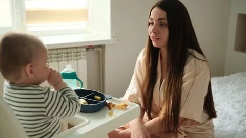 Loving mother interacting with her infant son as he sits in a high chair eating Stock-Footage 342951471