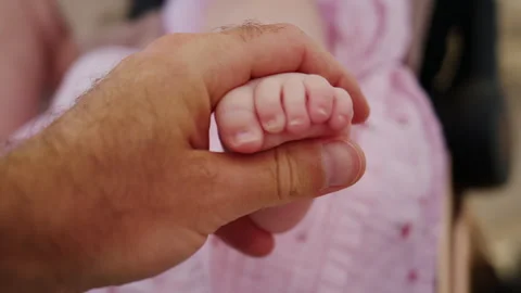 Loving parent hand gently caressing a baby's tiny foot, symbolizing new life, Stock Footage 339783877