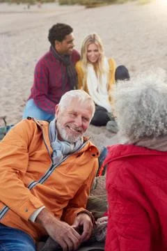 Loving Senior Couple Relaxing By Fire With Adult Offspring On Winter Beach Stock Photos