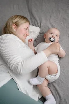 Loving young mother looking at newborn baby boy with pacifier in bed. Happy mom Stock Photos