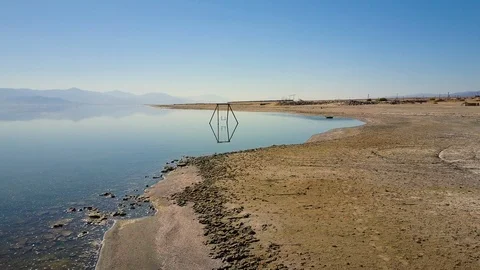 Low aerial camera passes over desolate ruins, shore of Bombay Beach, California Stock Footage 113483069