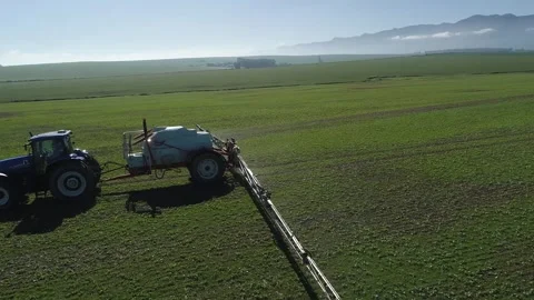 Low aerial circles tractor and sprayer spraying pesticide on green crop Stock Footage 304048467