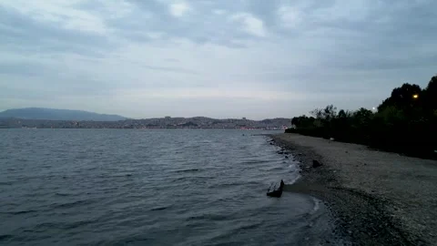Low Aerial Drone Flight Over a Rocky Shoreline with Izmir Cityscape at Dusk Stock Footage 319396369
