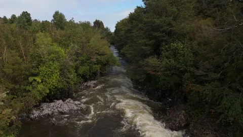 Low Aerial Flight Between Trees Over Turbulent Brown River in Lenca Chile Video stock 325245557