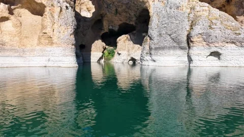 Low Aerial Flight Over Turquoise Lake Tilting Up Toward Cliff Caves Stock Footage 340111004