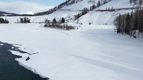 Low aerial over emerald river and snowbanks in Xinjiang winter valley Stock Footage 336609330