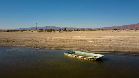 Low aerial over half sunken abandoned boat on the shore of Bombay Beach Stock Footage 113483662