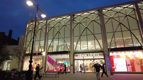 Low aerial view of John Lewis store at night with children skateboarding Stock Footage