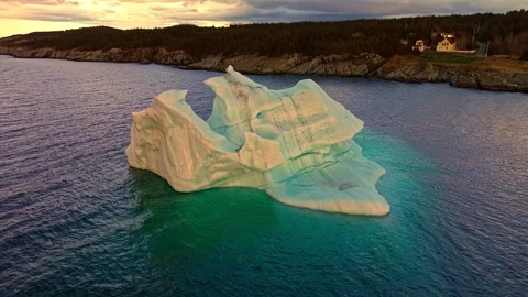 Low aerial view of wide flat iceberg floating near rocky Cupids shoreline at Stock Footage 336397232