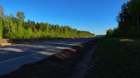 A low-altitude, angled flight crossing a newly paved road by pine forest Stock Footage 344401407