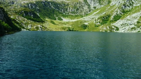 Low-altitude drone flight over mountain lake with rocky and green shores Stock Footage 314198499
