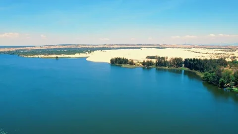 Low altitude drone push over a green oasis lake and wind turbines 4K Stock Footage 338369440