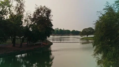Low altitude drone tracking forward while ascending over green lake and wooden Stock Footage 333343692
