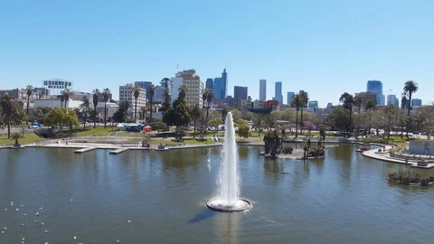 Low altitude rising drone shot of McArthur Park fountain and LA skyline Video stock 127984341